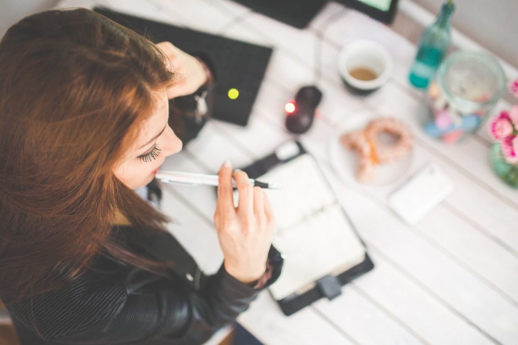 Une femme avec un stylo à la main devant un agenda sur un bureau